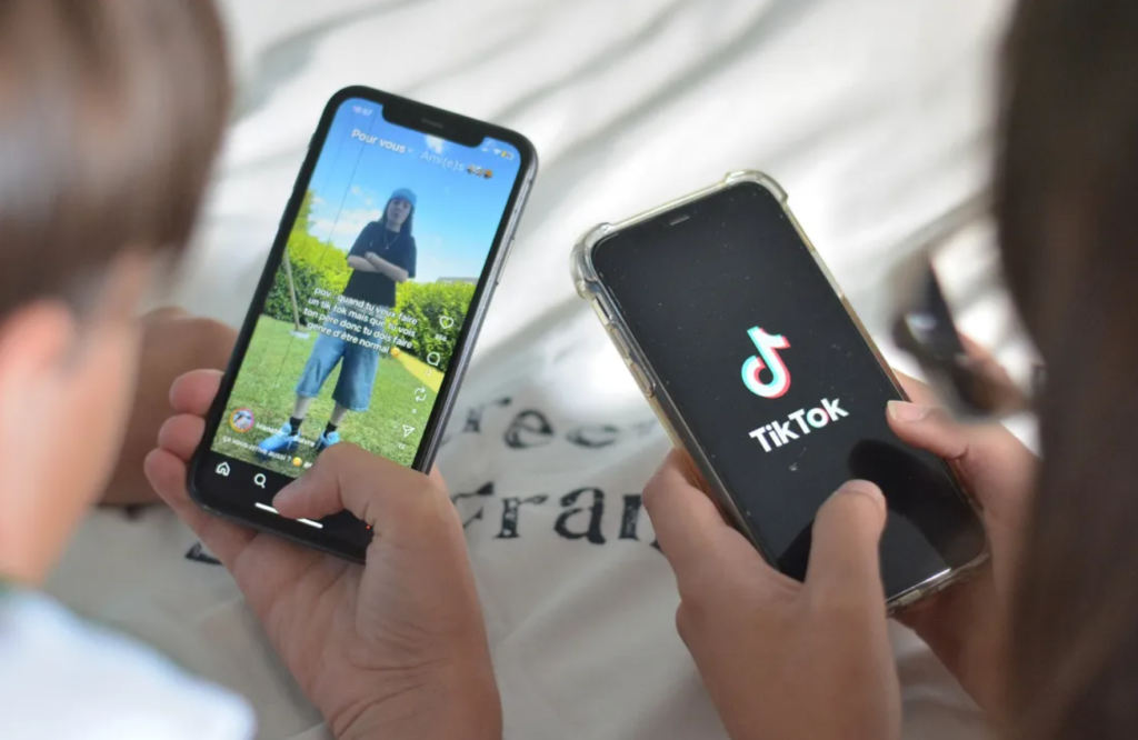 Deux adolescents sur tiktok. Seul leurs mains et une partie de leur tête est visible, leur téléphone ouverts sur tiktok sont clairs. 